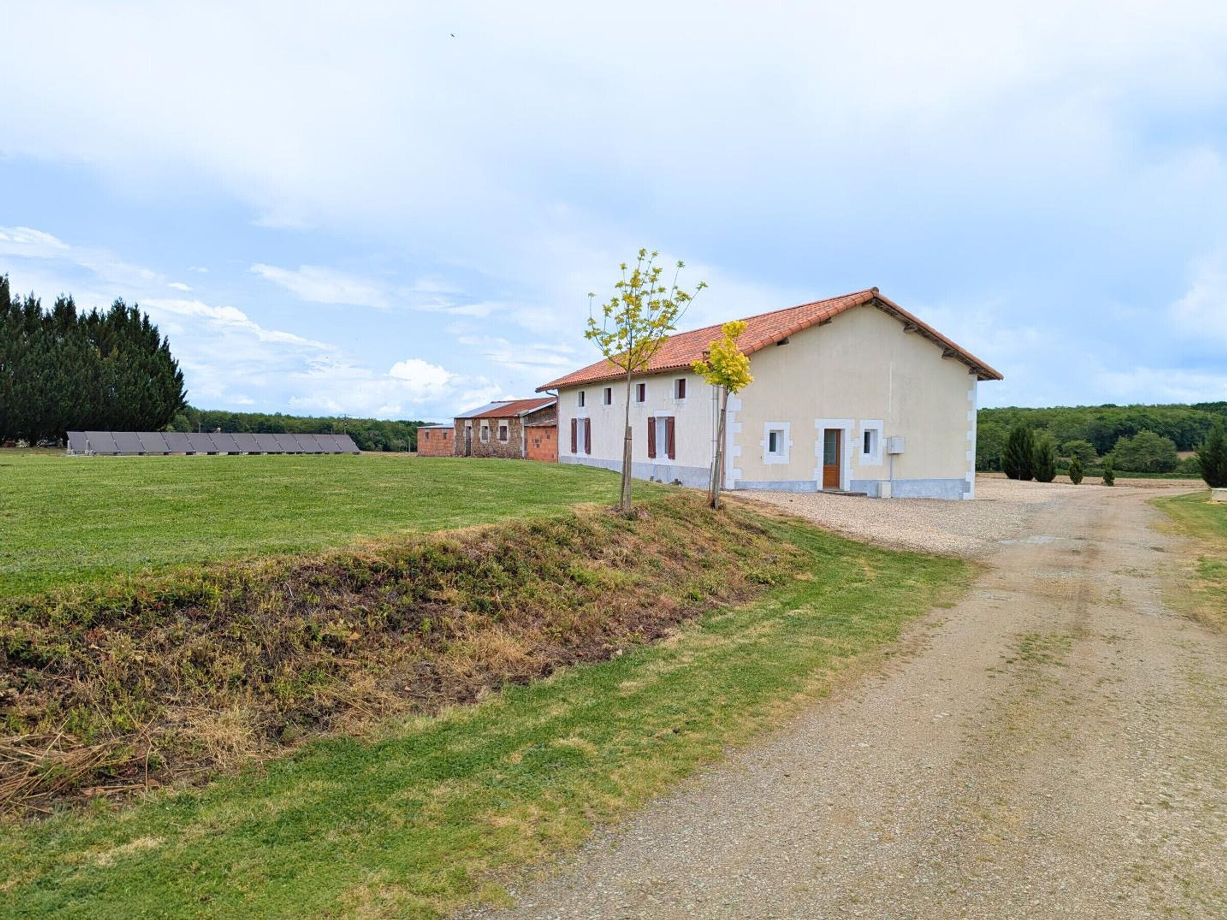 Una propiedad rural con un extenso campo abierto, un camino de entrada de grava y un edificio con tejado de tejas rojas.