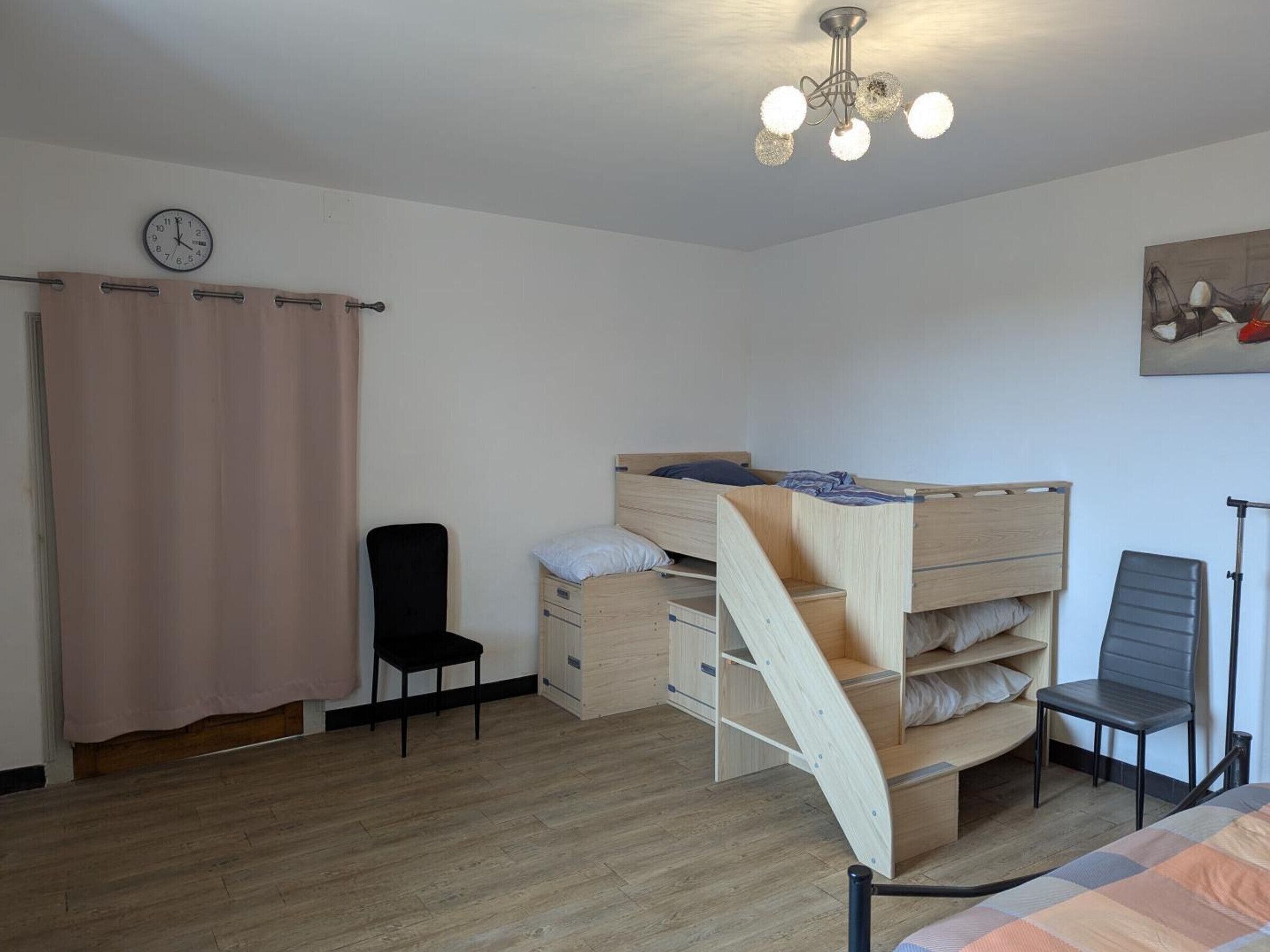 Un dormitorio con una litera, un escritorio, una silla, un reloj y una lámpara en el techo.
