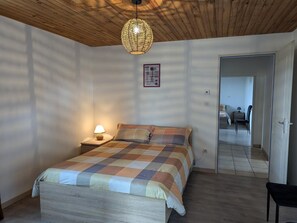 A bedroom with a wooden ceiling, a bed with a checkered bedspread, a bedside lamp, and a hanging light fixture.