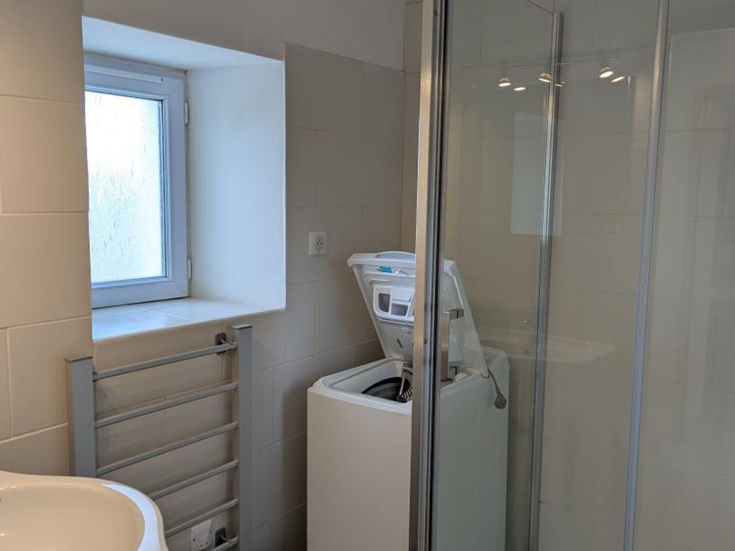 A bathroom with a window, a glass shower enclosure, and a white washing machine.