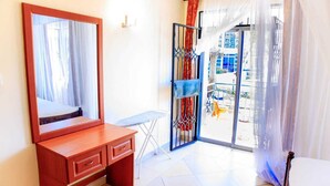 A bedroom with a wooden dresser, a mirror, and a sliding glass door leading to a balcony.
