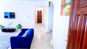 A living room with a blue sofa, a flat-screen TV mounted on the wall, and a wooden door with a painting.