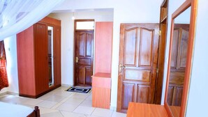 A bedroom with a bed, a wooden wardrobe, a wooden door, and a small table.
