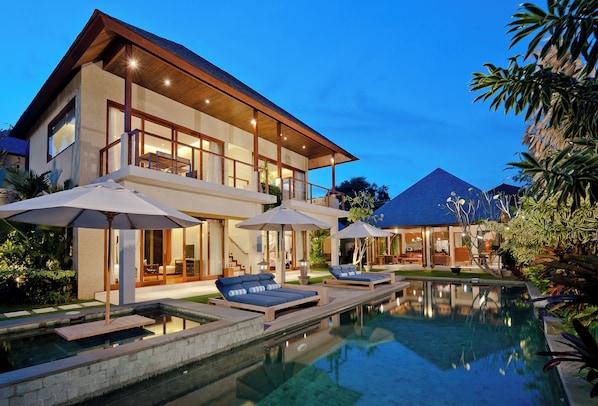 A modern house with a swimming pool, lounge chairs, and umbrellas.