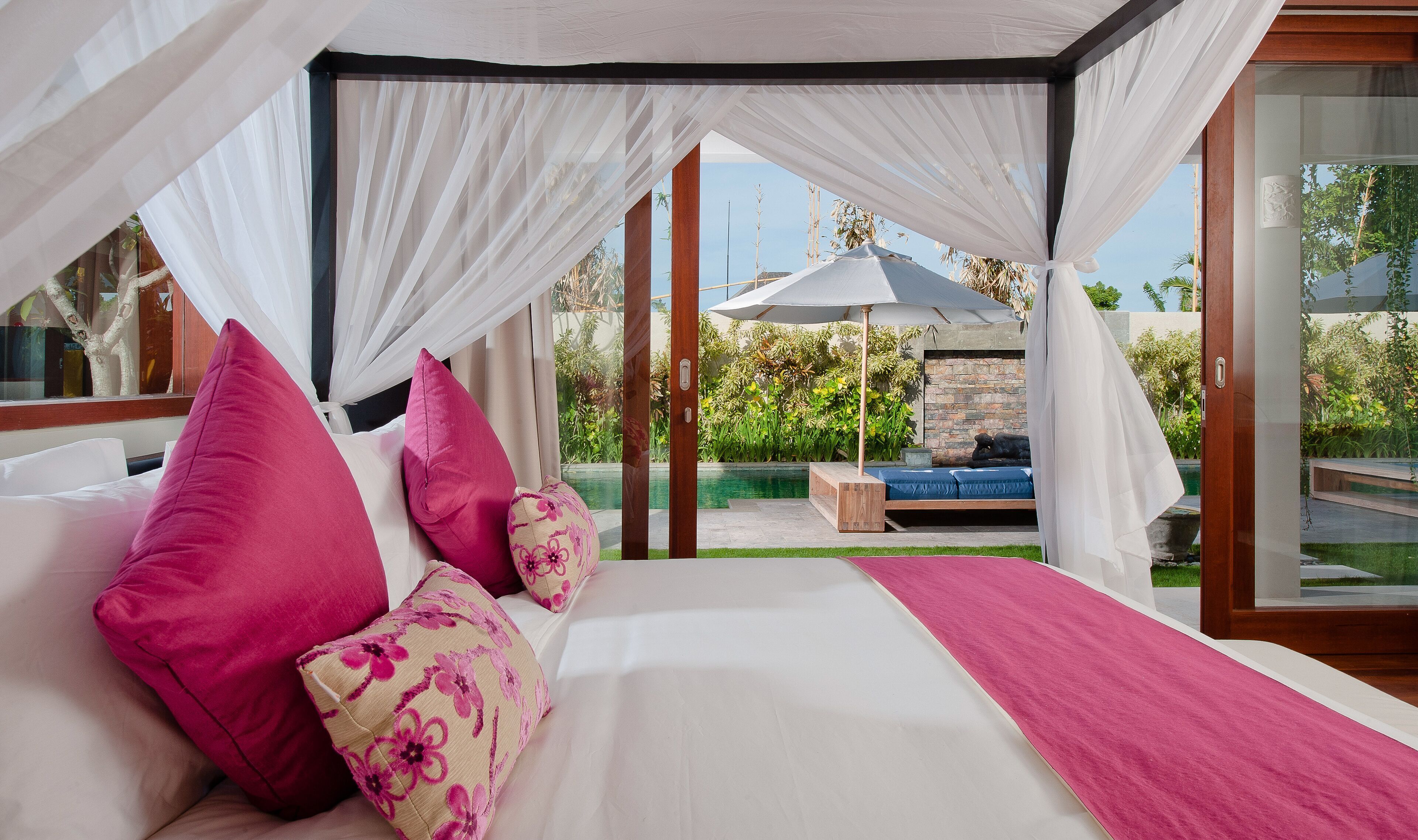 Une chambre à coucher avec un lit à baldaquin, une vue sur le jardin et un coin salon agrémenté d’un parasol.