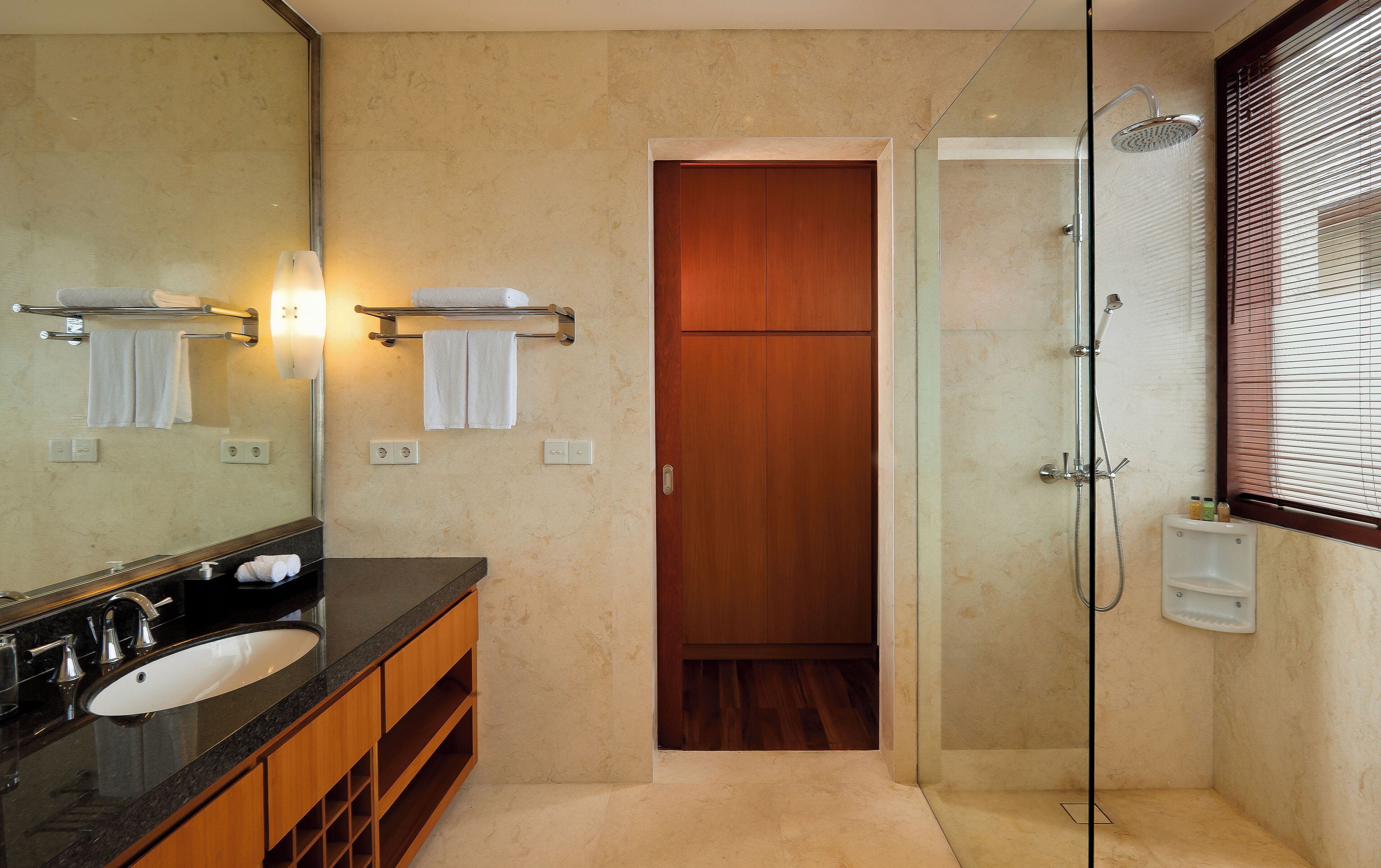 Une salle de bain moderne avec un grand miroir, un lavabo, une douche et une porte en bois.