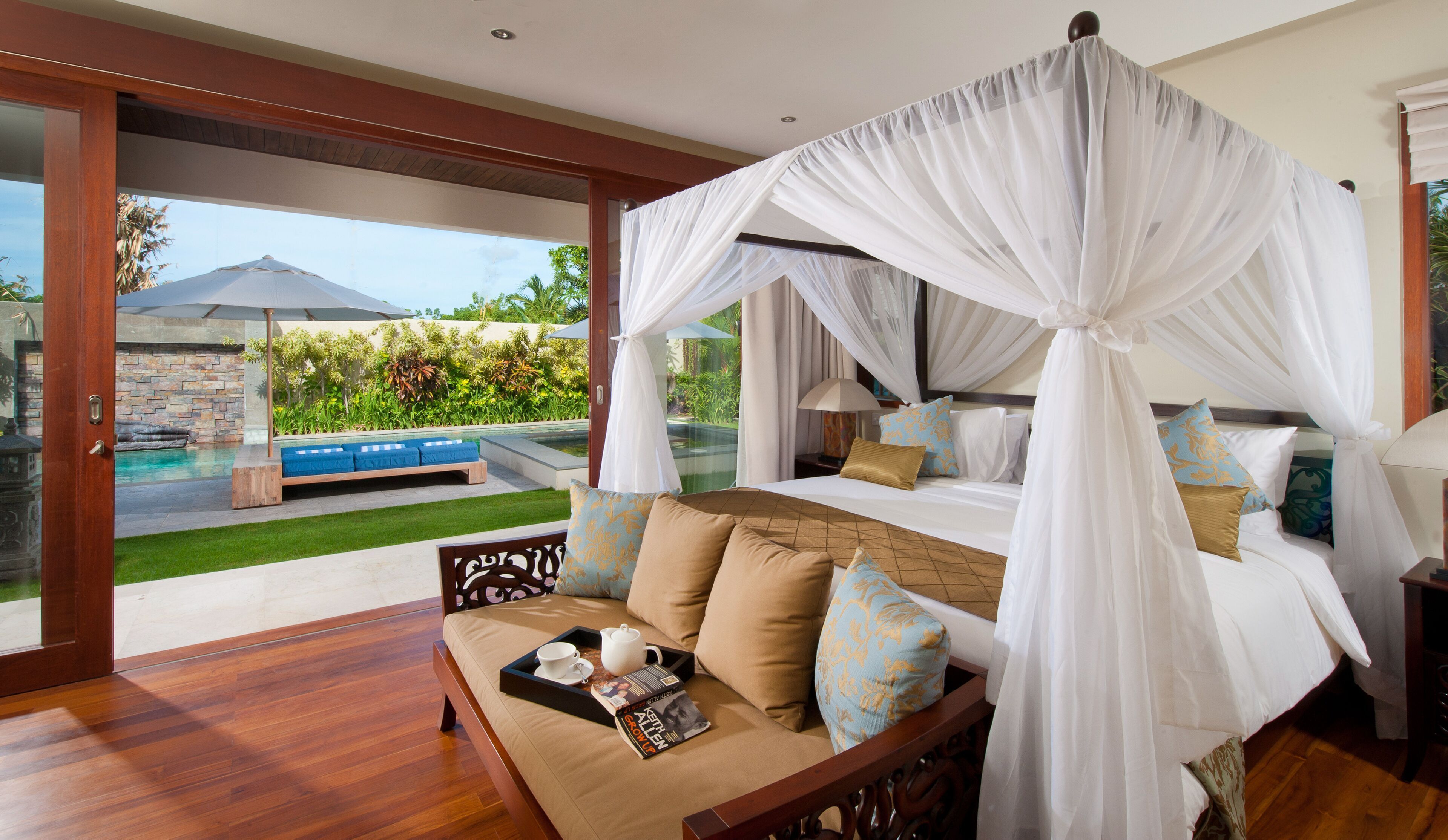 Une chambre avec un lit à baldaquin, un canapé doté d’une petite table et une vue sur une piscine et un espace de détente extérieur.