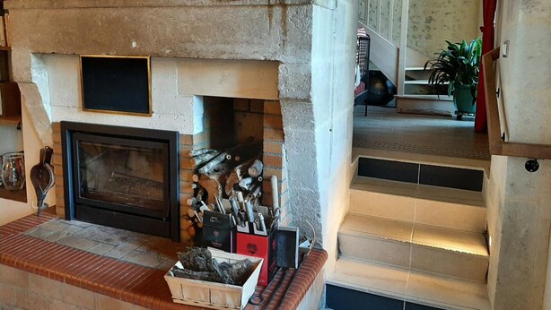 Una chimenea con repisa de piedra, una caja de madera con leña y una caja de metal con utensilios para la chimenea.