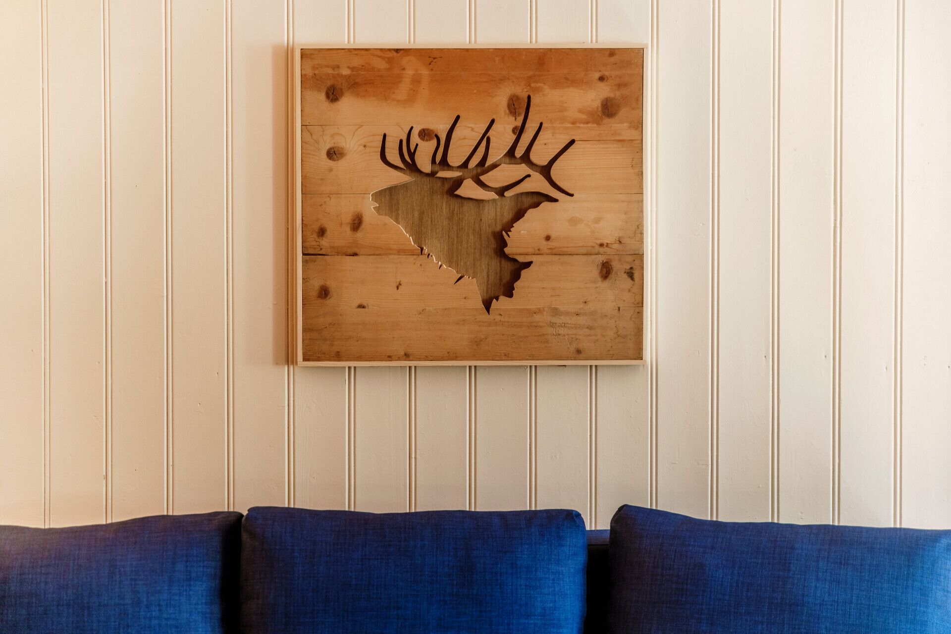 Un pannello decorativo in legno raffigurante un cervo appeso a una parete con rivestimento a listelli verticali.