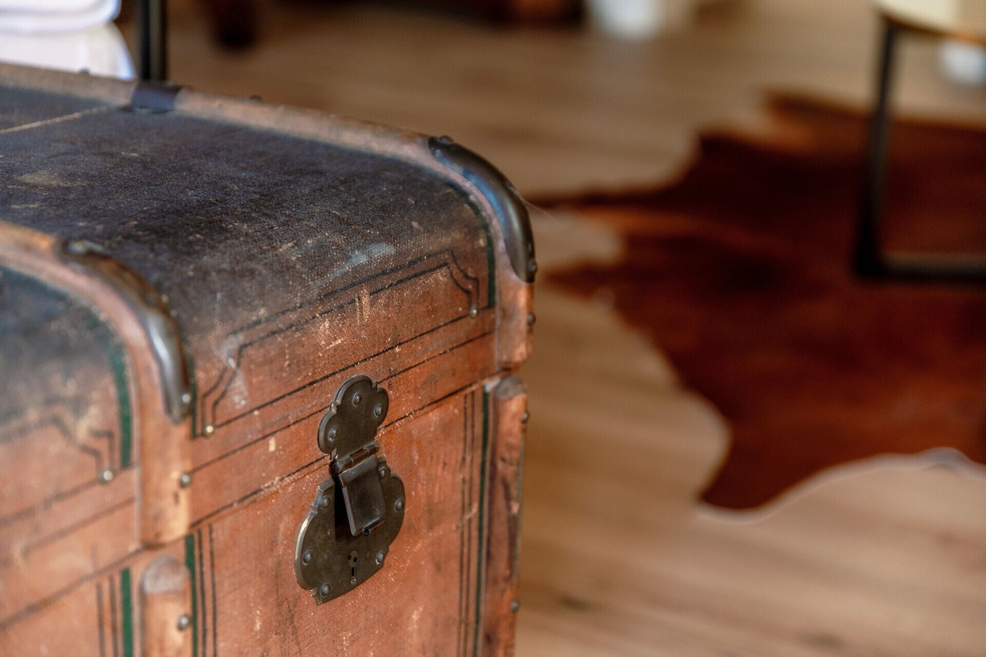 A close-up of a vintage suitcase with a metal latch, placed on a wooden floor.