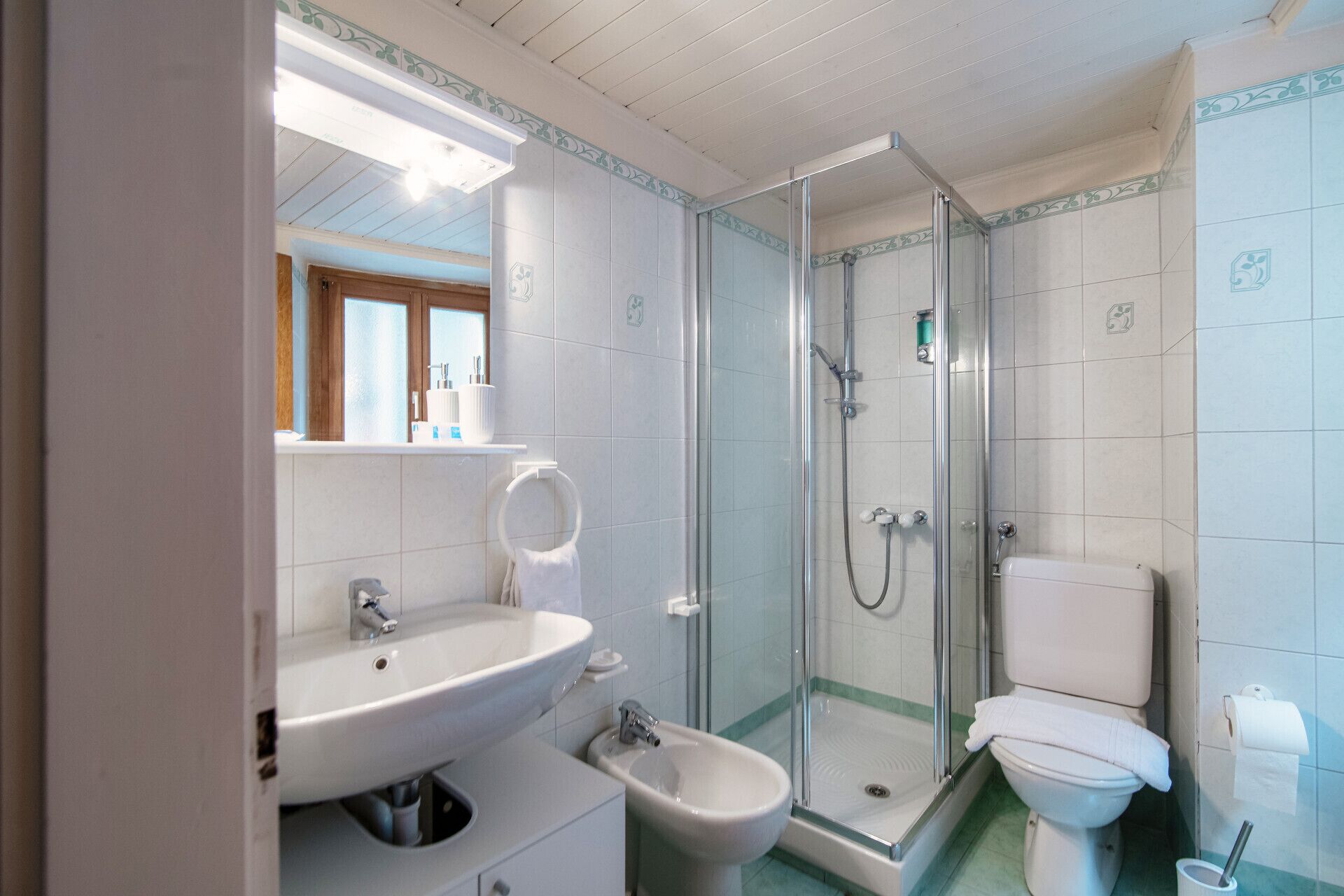 A bathroom with a sink, bidet, toilet, and glass-enclosed shower.