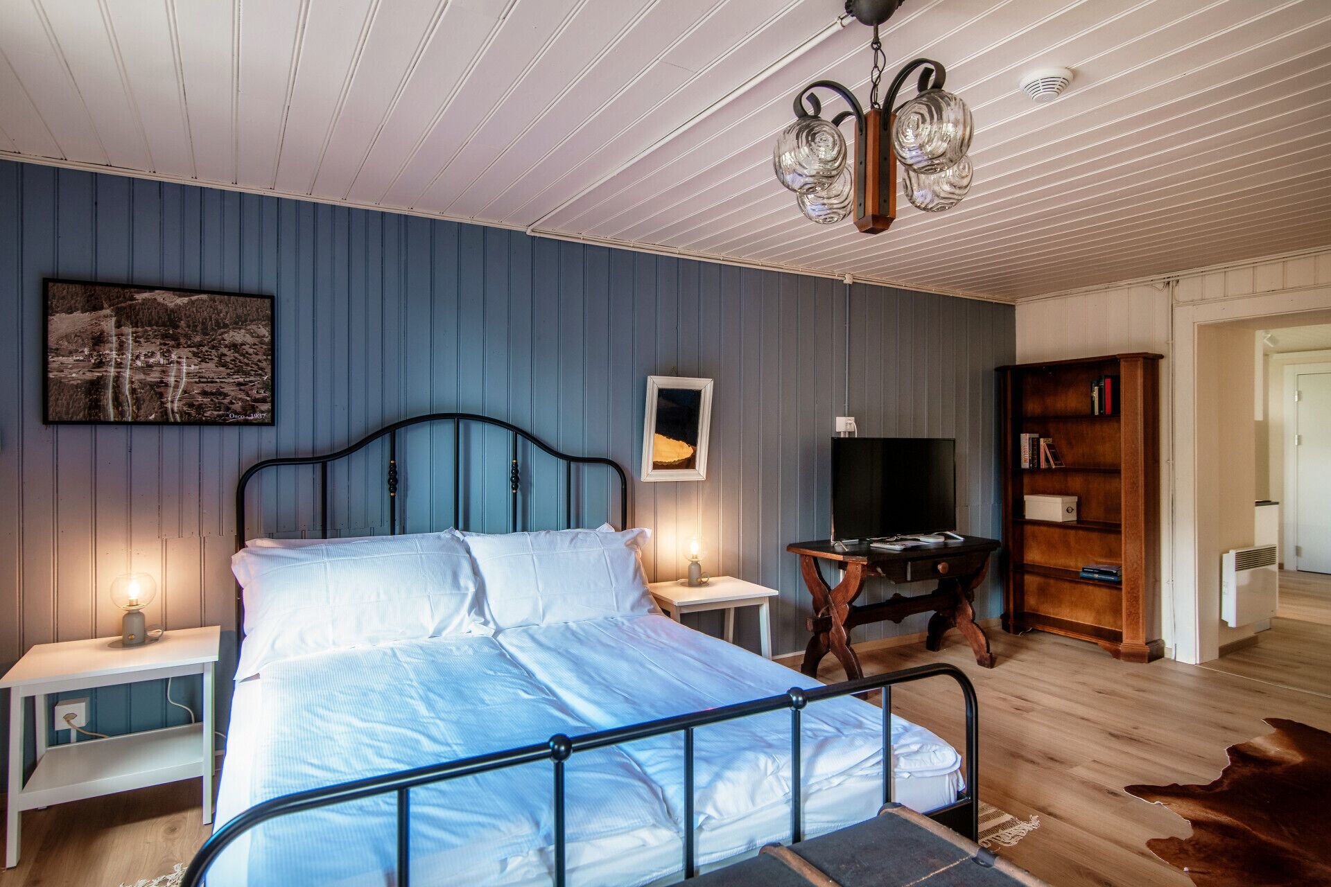 Une chambre à coucher comprenant un lit, des tables de chevet, un téléviseur, une bibliothèque et un luminaire au plafond.