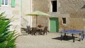 Une cour avec une table et des chaises, une petite table de ping-pong et un parasol vert.