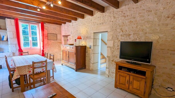 Un salon chaleureux avec une table en bois, des chaises, un téléviseur posé sur un meuble en bois et un mur en pierre.