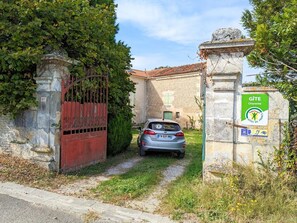 Een auto geparkeerd bij een poort met een stenen muur, een bordje geeft een vakantieverblijf in Charente aan.