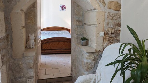 A stone archway leading to a bedroom with a bed, a small shelf with a plant, and a white cat figurine on the floor. - Renovated house near Angoulême with private garden (Vindelle)