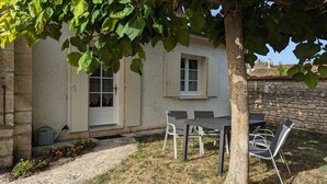 A stone building with a white door and window shutters, a table and chairs outside, and a tree in the foreground. - Renovated house near Angoulême with private garden (Vindelle)