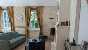Ein Wohnzimmer mit einer Couch, einem Couchtisch und einem Fernseher. Eine Steinwand und ein Fenster mit Vorhängen sind ebenfalls zu sehen.