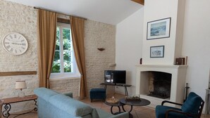 Ein Wohnzimmer mit einer Couch, zwei Sesseln, einem Fernseher, einem Kamin und einer Wanduhr.