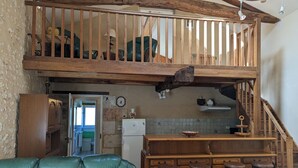 A rustic kitchen with a wooden staircase, a green leather sofa, and a bar area with stools. - Charming stone cottage in Bellon with garden, fireplace and internet (Bellon)