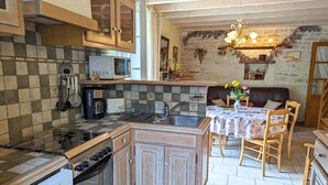 Een compacte keuken met een centraal eiland, houten kastjes, en een eethoek met een tafel en stoelen.