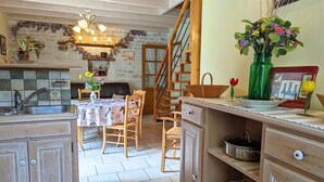 Een landelijke keuken met houten kastjes, een eettafel met stoelen, en een trap naar een hoger niveau.