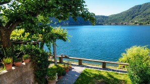 Un jardin au bord du lac, avec un sentier en pierre, des plantes en pot et une balustrade en bois donnant sur un lac paisible.
