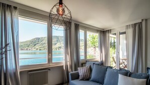 Une pièce dotée d’une grande fenêtre donnant sur un lac et des collines, d’un canapé avec des coussins et d’un radiateur.