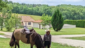 A person with a horse in a grassy area with a house and trees in the background. - Spacious Stone House with Shared Pool, Babyfoot, and Nature Trails in Bucolic Setting (Montmoreau)