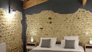 A bedroom with a stone wall, wooden beams, a bed with pillows, and bedside lamps. - Spacious Stone House with Shared Pool, Babyfoot, and Nature Trails in Bucolic Setting (Montmoreau)