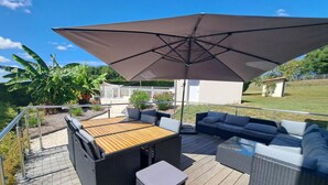 An outdoor patio area with a wooden deck, wicker furniture, and a large umbrella providing shade. - Spacious Stone House with Shared Pool, Babyfoot, and Nature Trails in Bucolic Setting (Montmoreau)