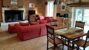 A living room with a fireplace, red sofas, a dining table with chairs, and a stone wall. - La Queue Rousse Cottage - Historic Home with Fireplace and Enclosed Garden (Vitrac-Saint-Vincent)