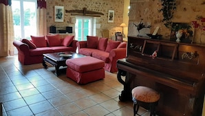 A cozy living room with a red sofa set, a wooden coffee table, and a piano. - La Queue Rousse Cottage - Historic Home with Fireplace and Enclosed Garden (Vitrac-Saint-Vincent)