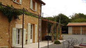A rustic stone building with multiple windows and doors, a covered outdoor seating area with tables and chairs, and a garden with climbing plants. - La Queue Rousse Cottage - Historic Home with Fireplace and Enclosed Garden (Vitrac-Saint-Vincent)