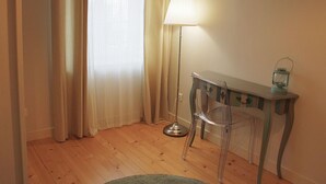 A room with wooden flooring, a desk with a lamp, a chair, and a small table with a lantern.