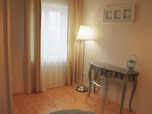 Una habitación con suelo de madera, un escritorio con lámpara, una silla y una pequeña mesa con farol.