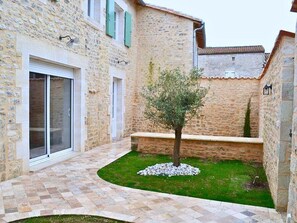 A stone building with a tiled patio, a small tree, and a grassy area.