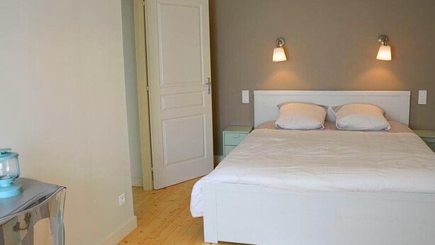 A bedroom with a large bed, two bedside lamps, and a door leading to another room.