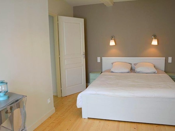 A bedroom with a large bed, two bedside lamps, and a door leading to another room.