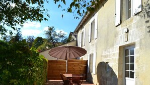 A patio with a wooden table and chairs, an umbrella, and a stone wall. - Family cottage in village, pets allowed (Salles-Lavalette)