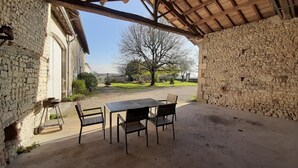 Un espacio al aire libre con patio, mesa y sillas, paredes de piedra y vistas a un paisaje rural.