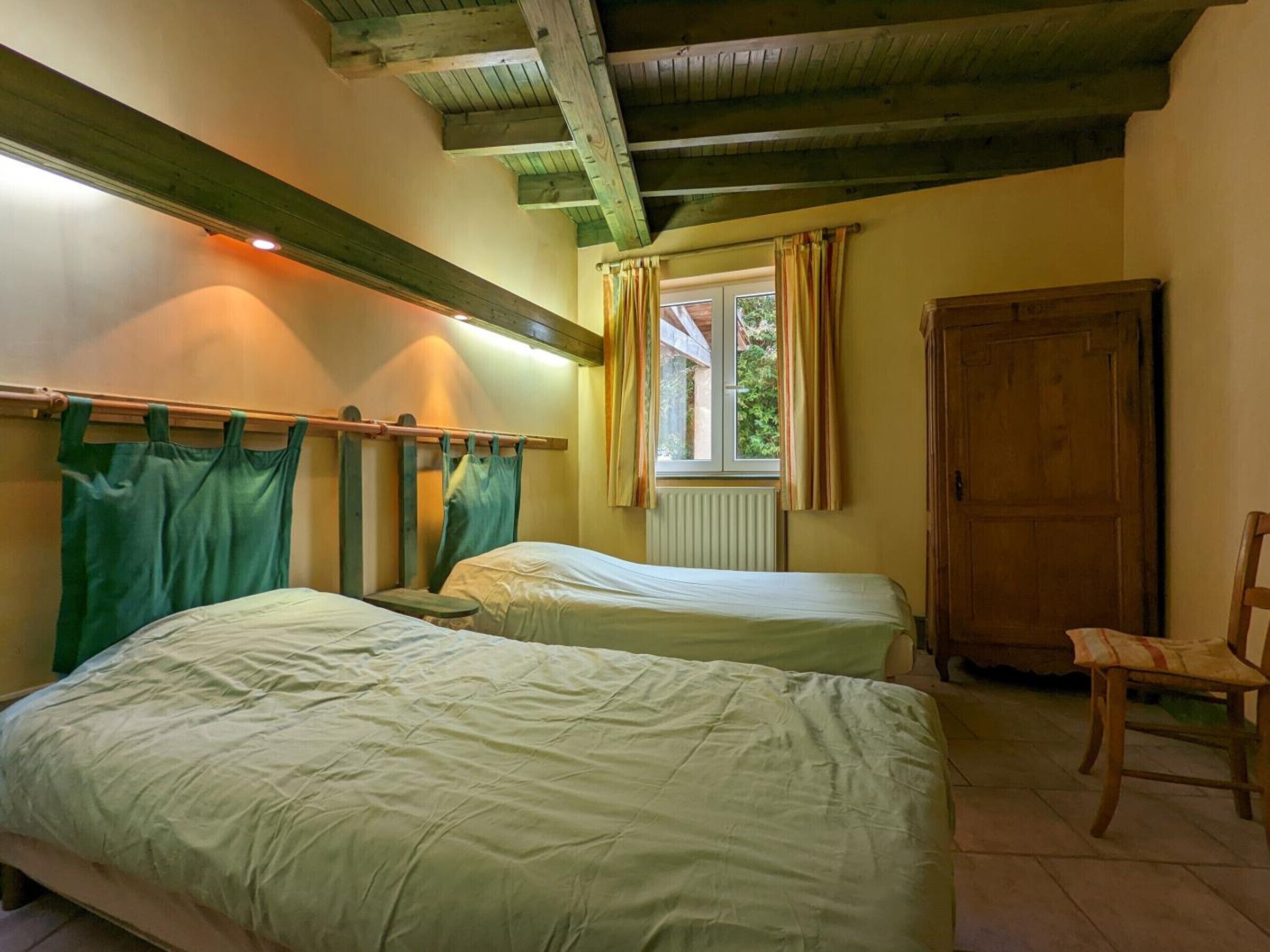 Een kamer met twee bedden, een houten stoel, een raam met gordijnen en een radiator.