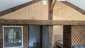 A rustic wooden interior with a loft bed, a framed cityscape painting, and a simple chair. - Charming Cottage with Heated Pool and Private Garden in Charras, Near Périgord (Charras)