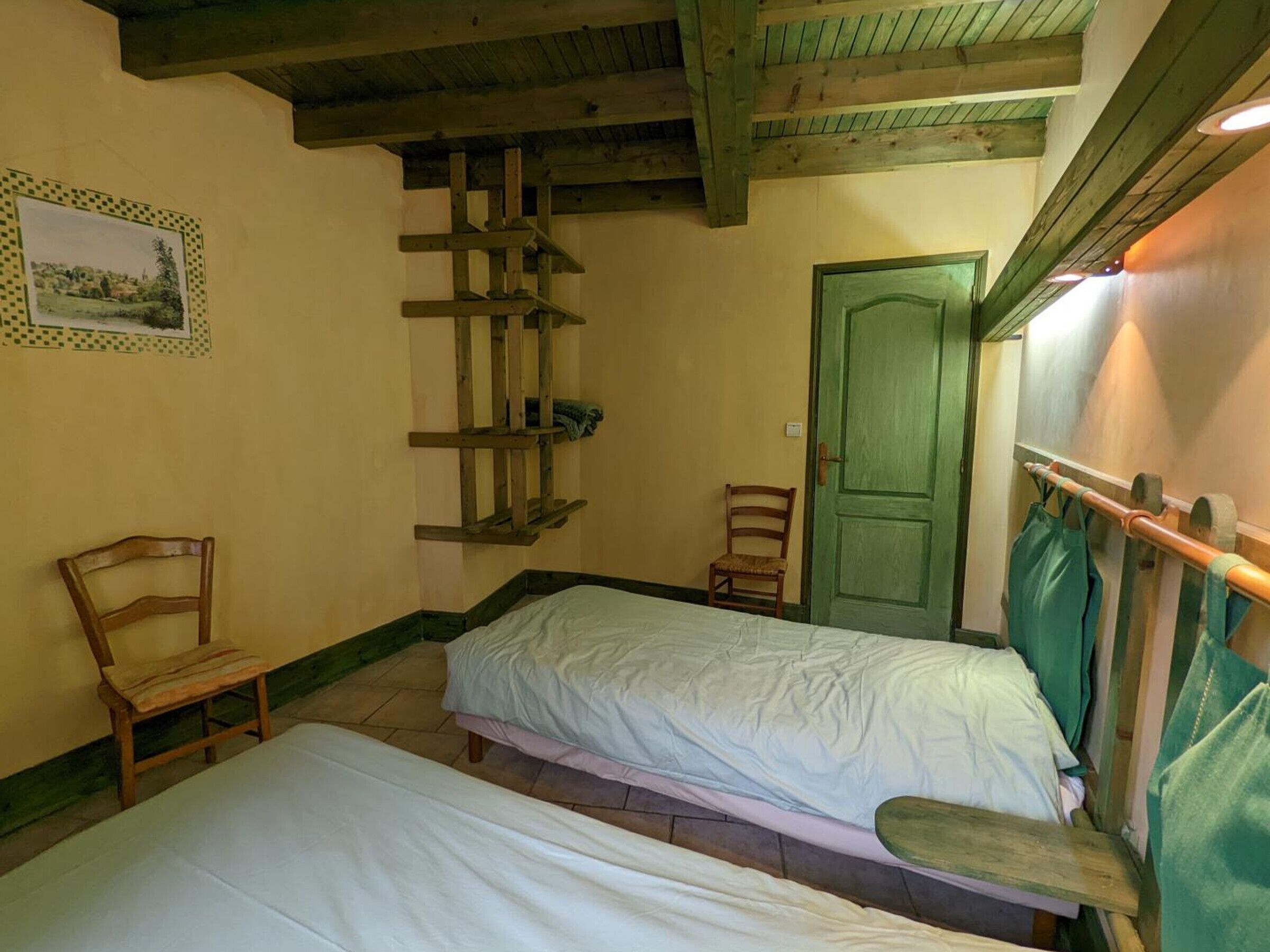 A room with two beds, a wooden chair, a door, and a wooden beam structure.