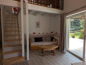 Una habitación con un sofá, una mesa de madera, una pared a cuadros, un cartel y vistas al exterior.