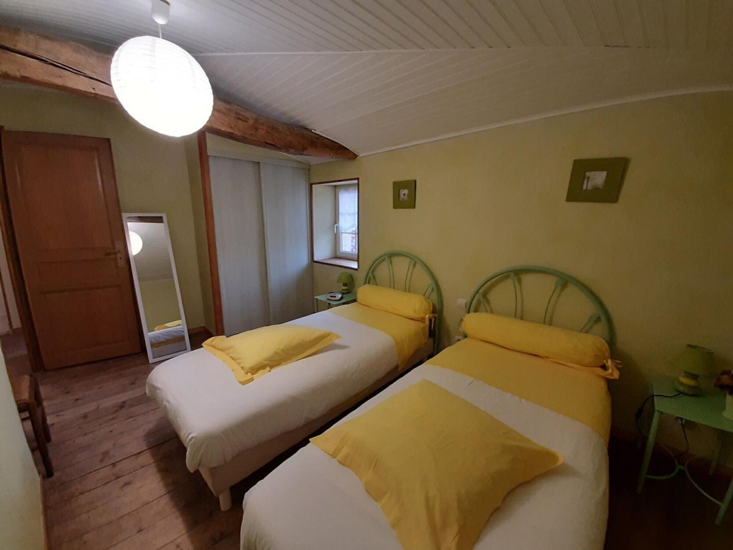 A room with two beds, wooden flooring, a mirror, a window, and a door.