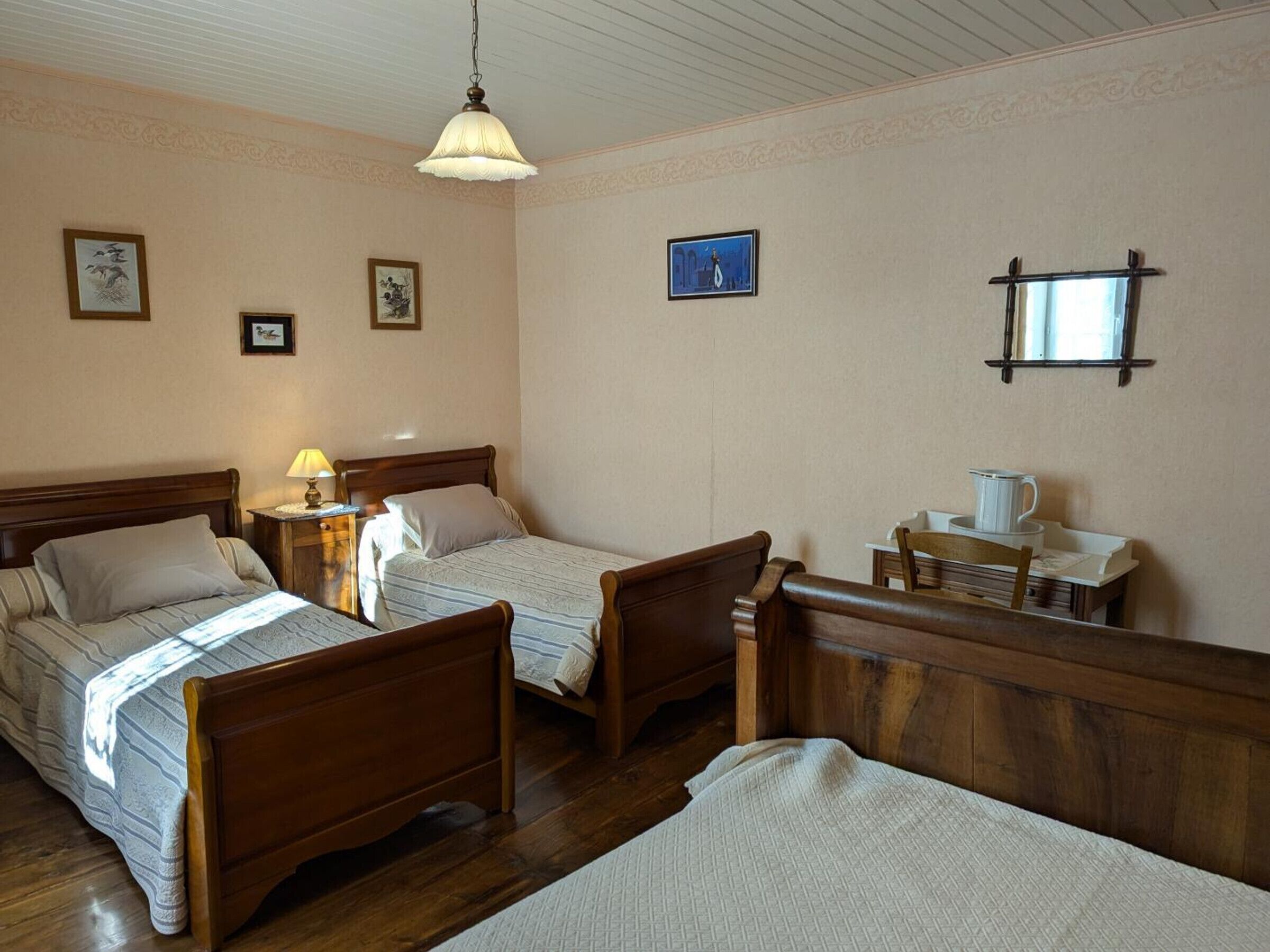 Une pièce avec deux lits en bois, une petite table avec une lampe et un miroir au mur.