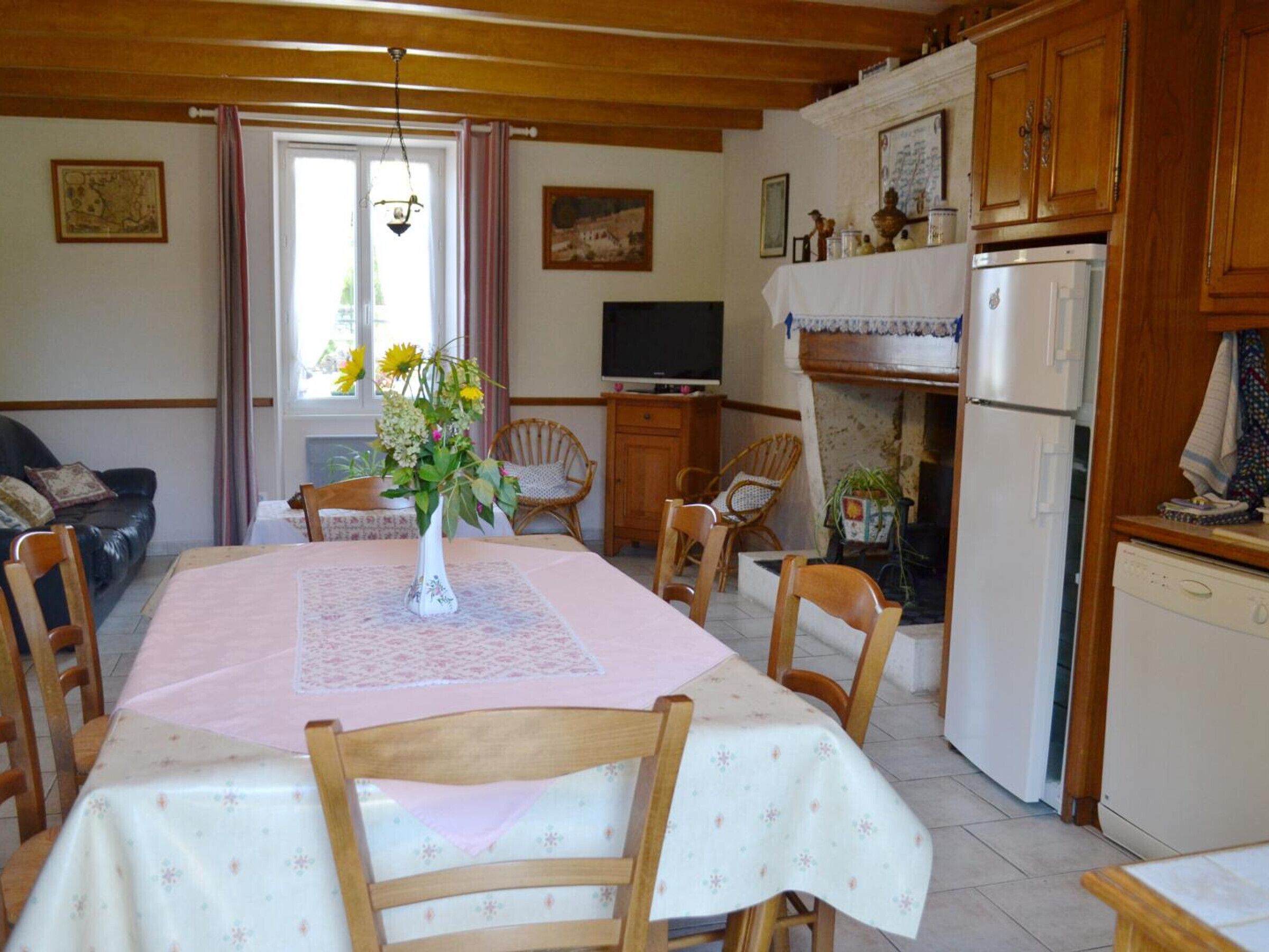 A cozy dining area with a table set for four, surrounded by wooden chairs. A vase with flowers is placed on the table, and a television is mounted on the wall.