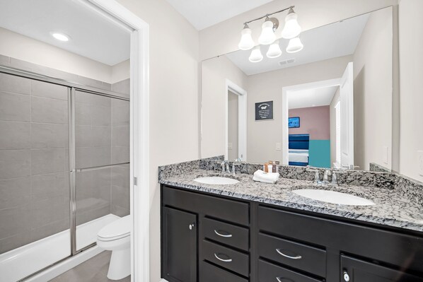 A modern bathroom with two sinks, a shower, and a toilet.