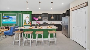 Een moderne keuken met een groene accentmuur, een groot eiland met barstoelen, roestvrijstalen apparatuur en hanglampen.
